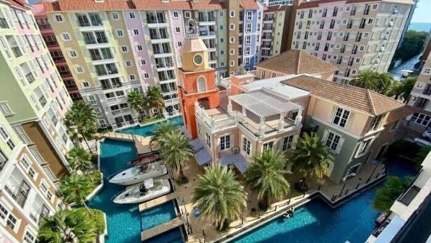 A multi-story hotel with a central courtyard featuring a swimming pool, palm trees, and a boat dock. - Jomtien Seven Seas Cote D'Azure (Muang Pattaya)