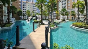 A resort with a central swimming pool, surrounded by palm trees and multi-story buildings. - Jomtien Seven Seas Cote D'Azure (Muang Pattaya)
