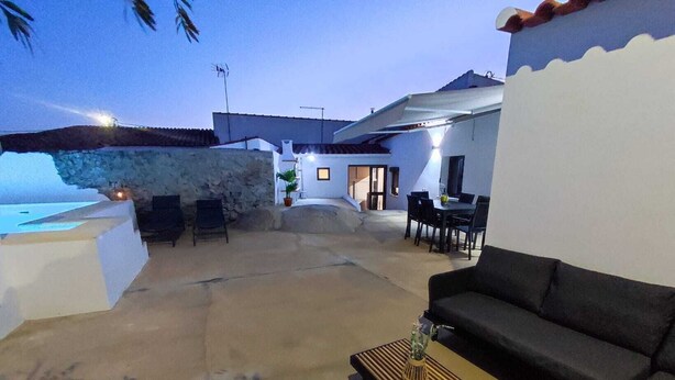 A spacious outdoor patio with a stone wall, a black sofa, a dining table, and a small wooden coffee table. - Casa da Pedra (Pedrogão)