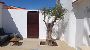A small outdoor seating area with a sofa and a coffee table, a brown door, and a tree. - Casa da Pedra (Pedrogão)