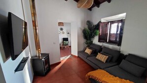 A living room with a sofa, a television, a fireplace, and a window with blinds. - Casa da Pedra (Pedrogão)