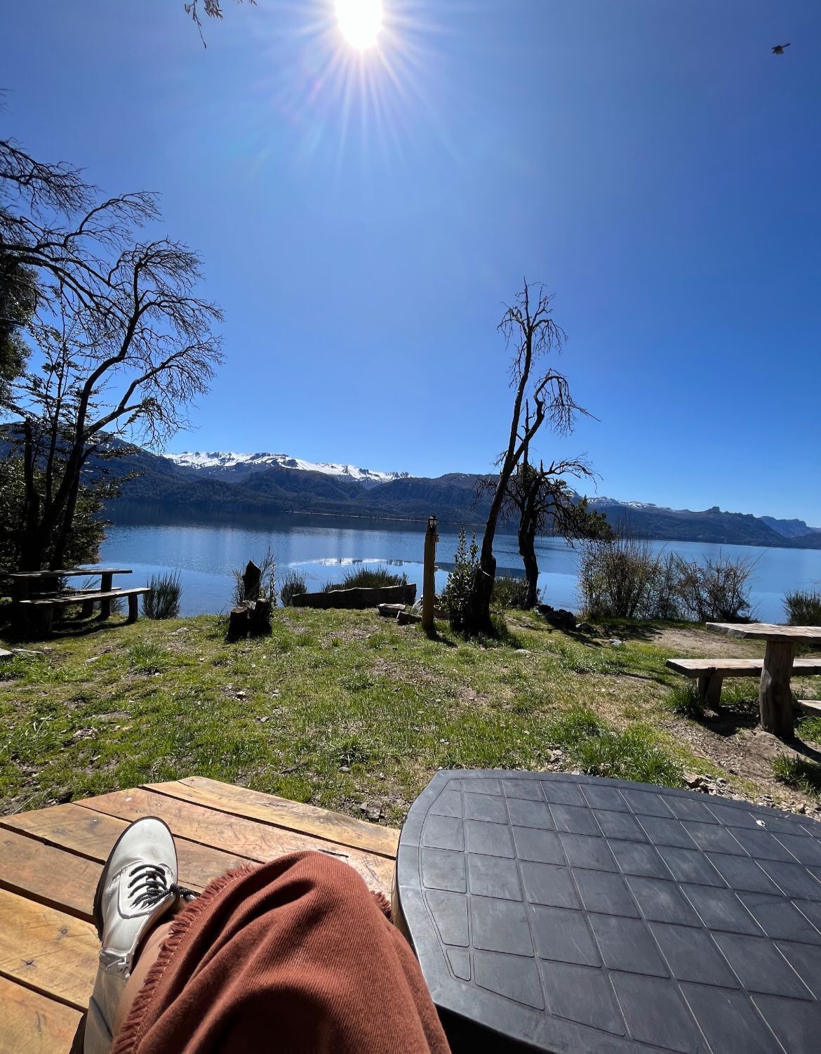 Vista de un lago con una mesa de picnic, un banco y una persona relajándose.