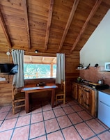 Una cabaña de madera con comedor, cocina y ventana con cortinas.