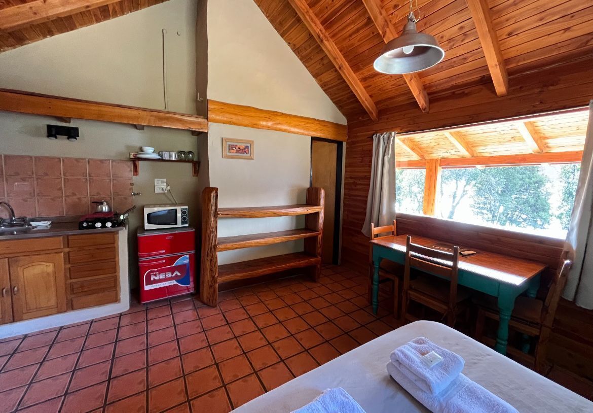 A rustic cabin with a kitchen, a dining area, and a large window.