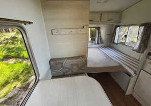 Un intérieur de camping-car compact comprenant un lit, un coin salon et une fenêtre donnant sur la verdure environnante.