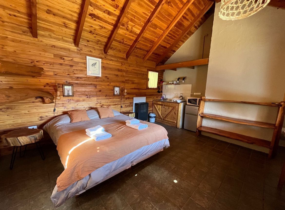 Un dormitorio rústico de cabaña con una cama grande, un escritorio pequeño y una kitchenette.