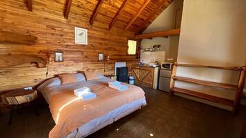Un dormitorio rústico de cabaña con una cama grande, un escritorio pequeño y una kitchenette.