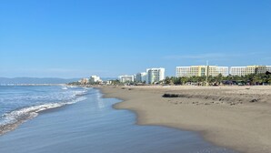 A beach with a clear sky, a sandy shore, and a row of multi-story buildings in the background.