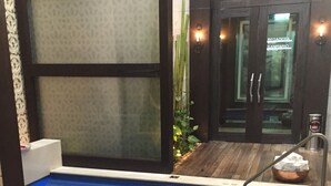 A small indoor pool with a tiled floor, surrounded by a wooden deck and a glass door leading to a room labeled "Região Sanitária."