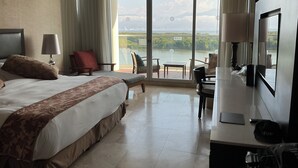 A hotel room with a large bed, a desk, and a TV. There is a balcony with a view of the city and mountains.