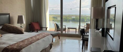 Habitación de hotel con una cama grande, un escritorio y un televisor. Tiene un balcón con vistas a la ciudad y a las montañas.