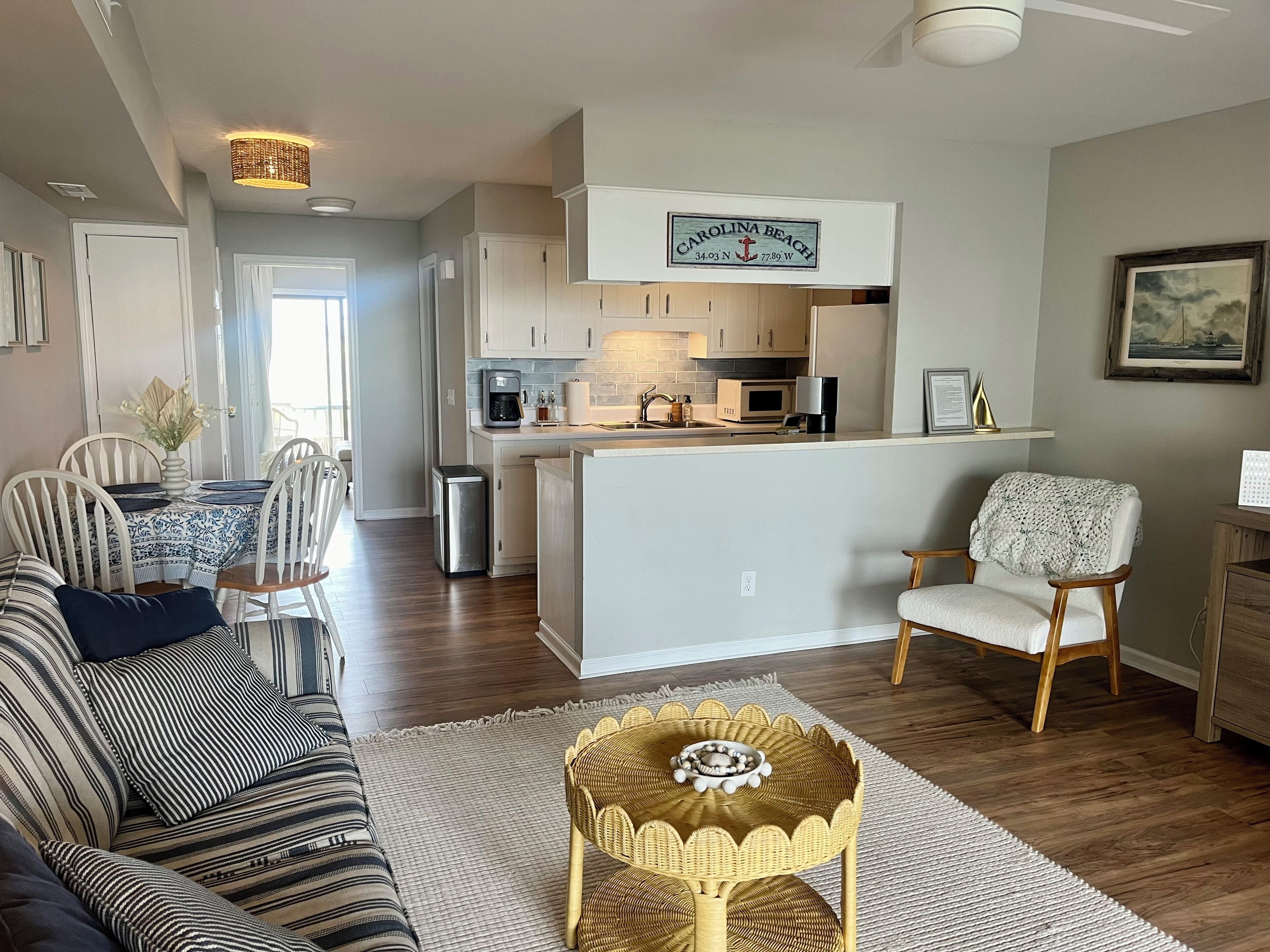 A modern kitchen with white cabinets, a coffee maker, and a microwave. There is a dining area with a striped sofa and a small round table.