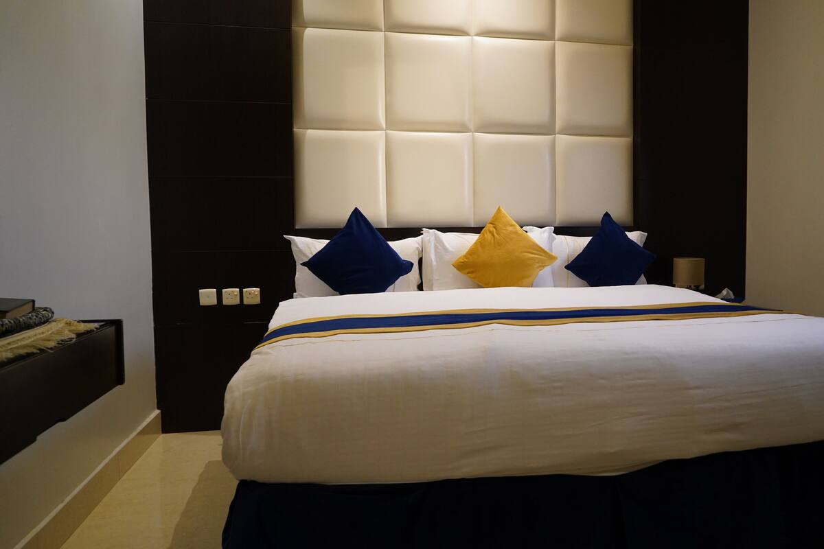 A hotel room with a large bed, a dark headboard, and a bedside table with a lamp.