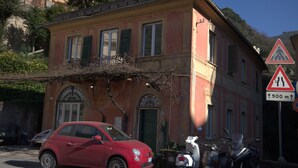 A red car parked in front of a building with a balcony and a pedestrian crossing sign nearby. - Bosmi Bed&Language Liguria (Sori)
