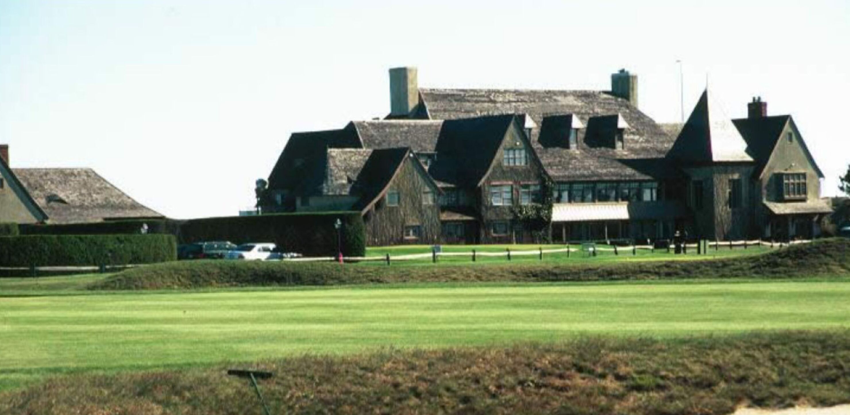 A large, traditional building with multiple gabled roofs, situated on a well-maintained lawn with a clear sky.