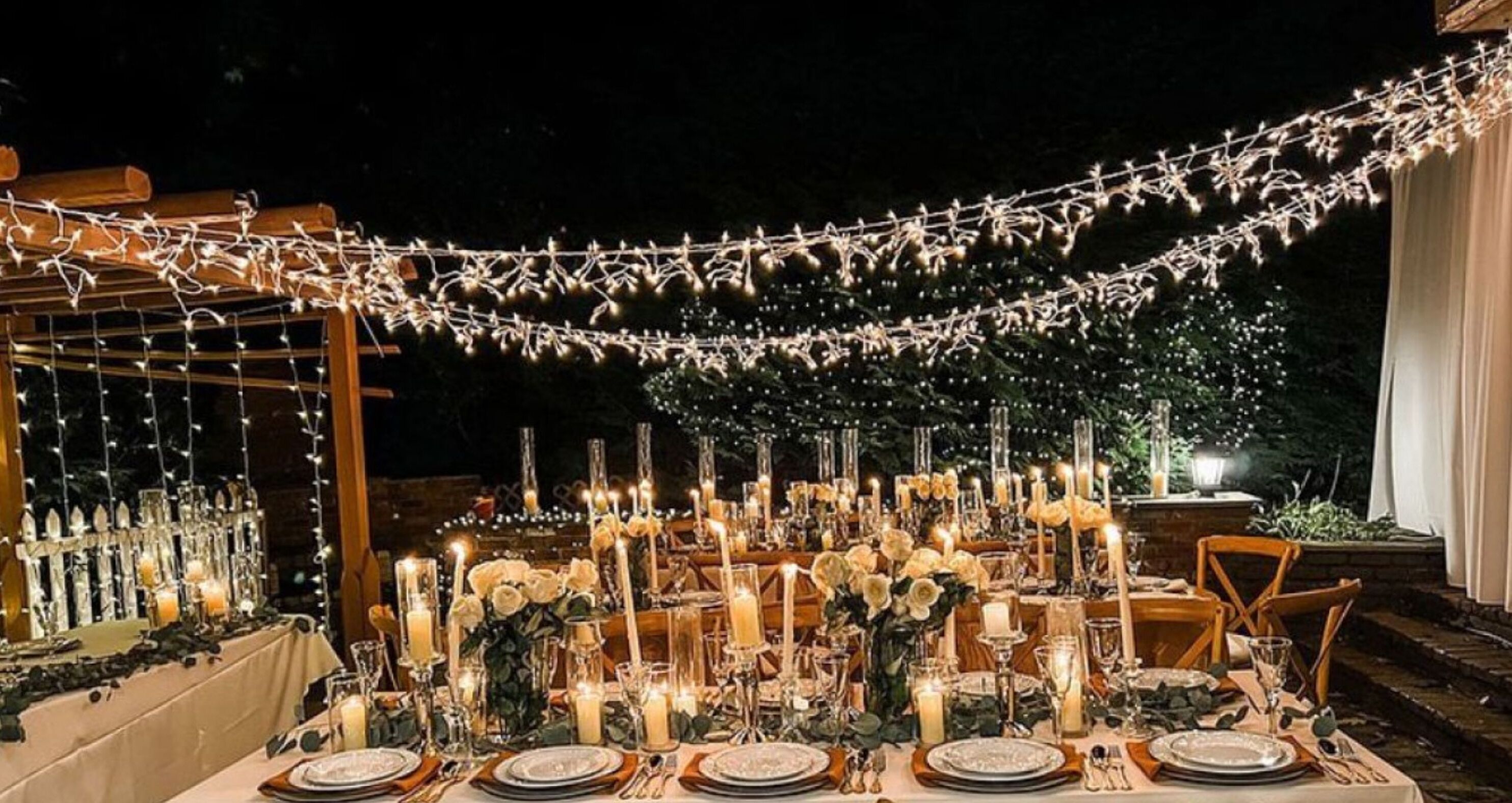 An outdoor dining area with string lights, candles, and tables set for a meal.