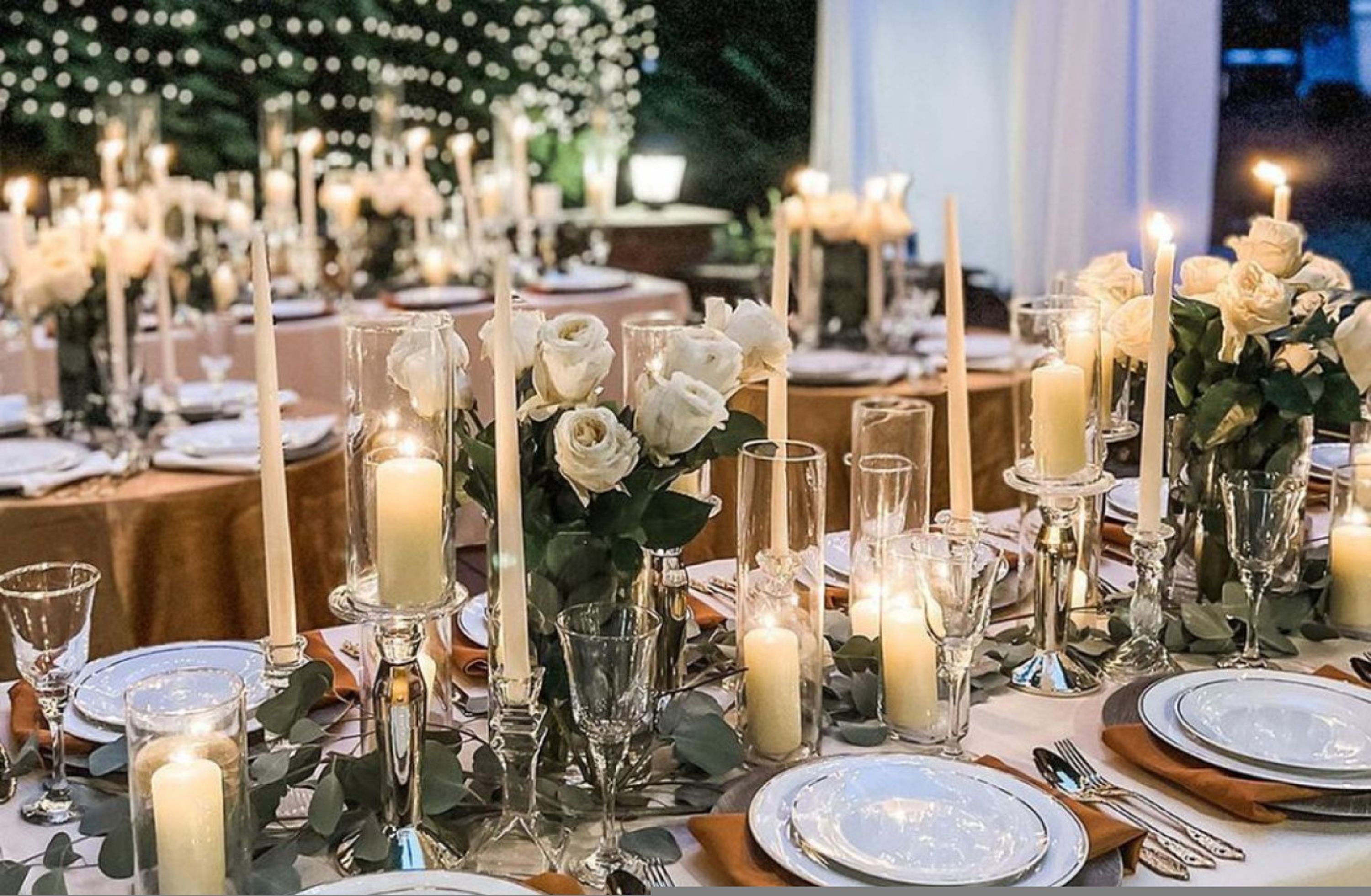 A formal dining setup with multiple tables, candles, and floral arrangements.