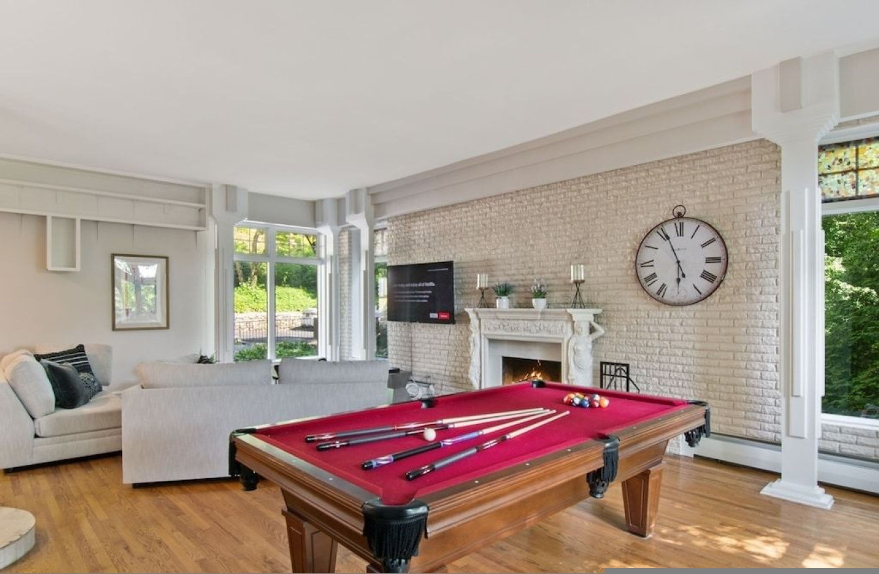 A billiards table with balls and cues, a sofa, a fireplace, and a clock on the wall.