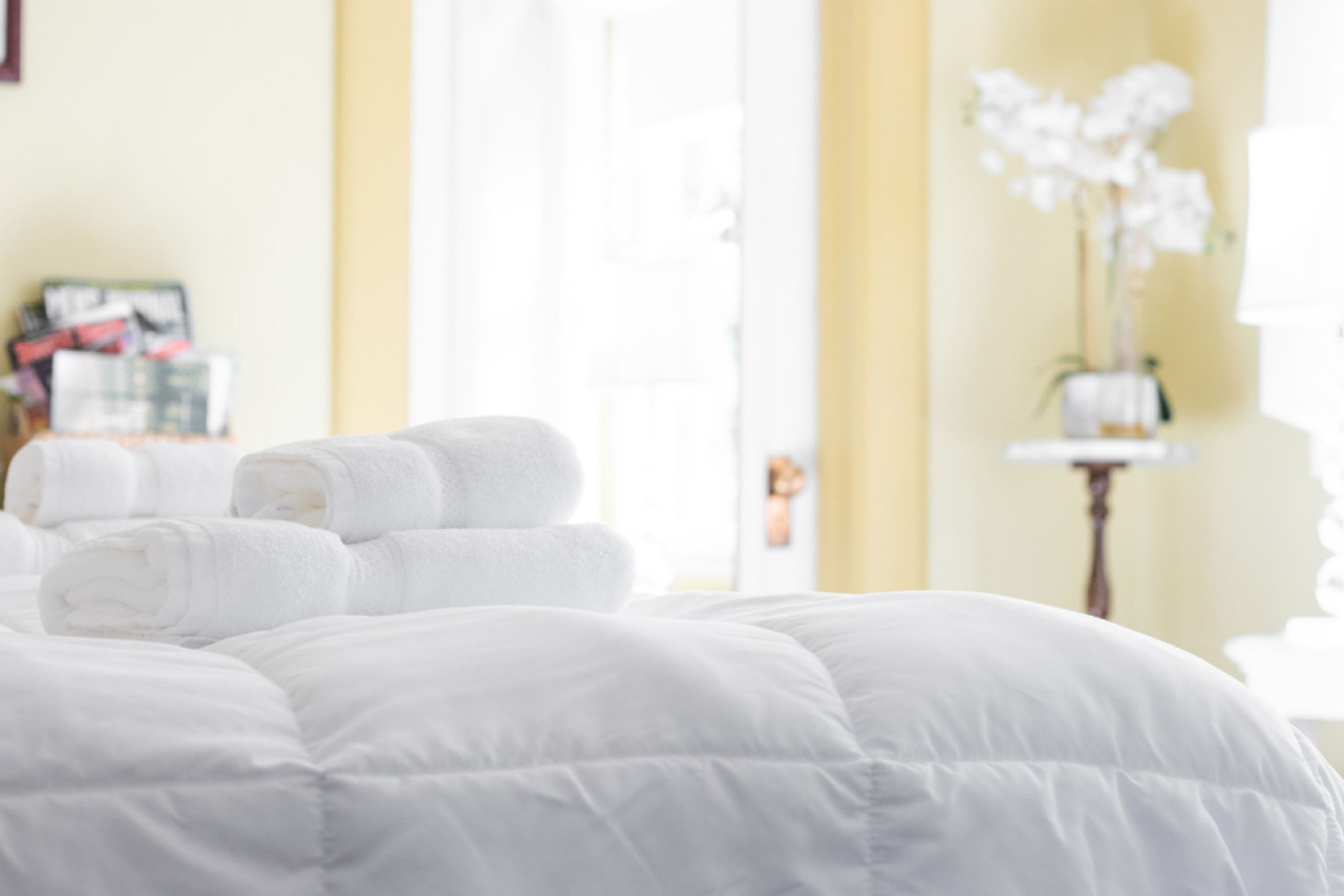 A neatly made bed with white bedding and rolled towels.