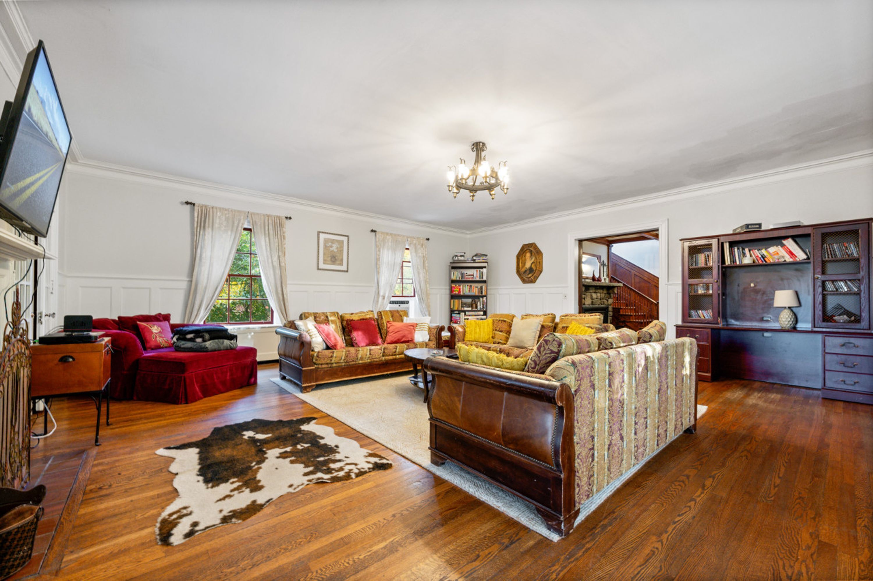 Amplia sala de estar con pisos de madera, un sofá de cuero grande, un sillón rojo, una mesa de centro de madera y una estantería.