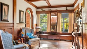 Un salon spacieux avec des boiseries, une cheminée et une grande fenêtre agrémentée de rideaux.