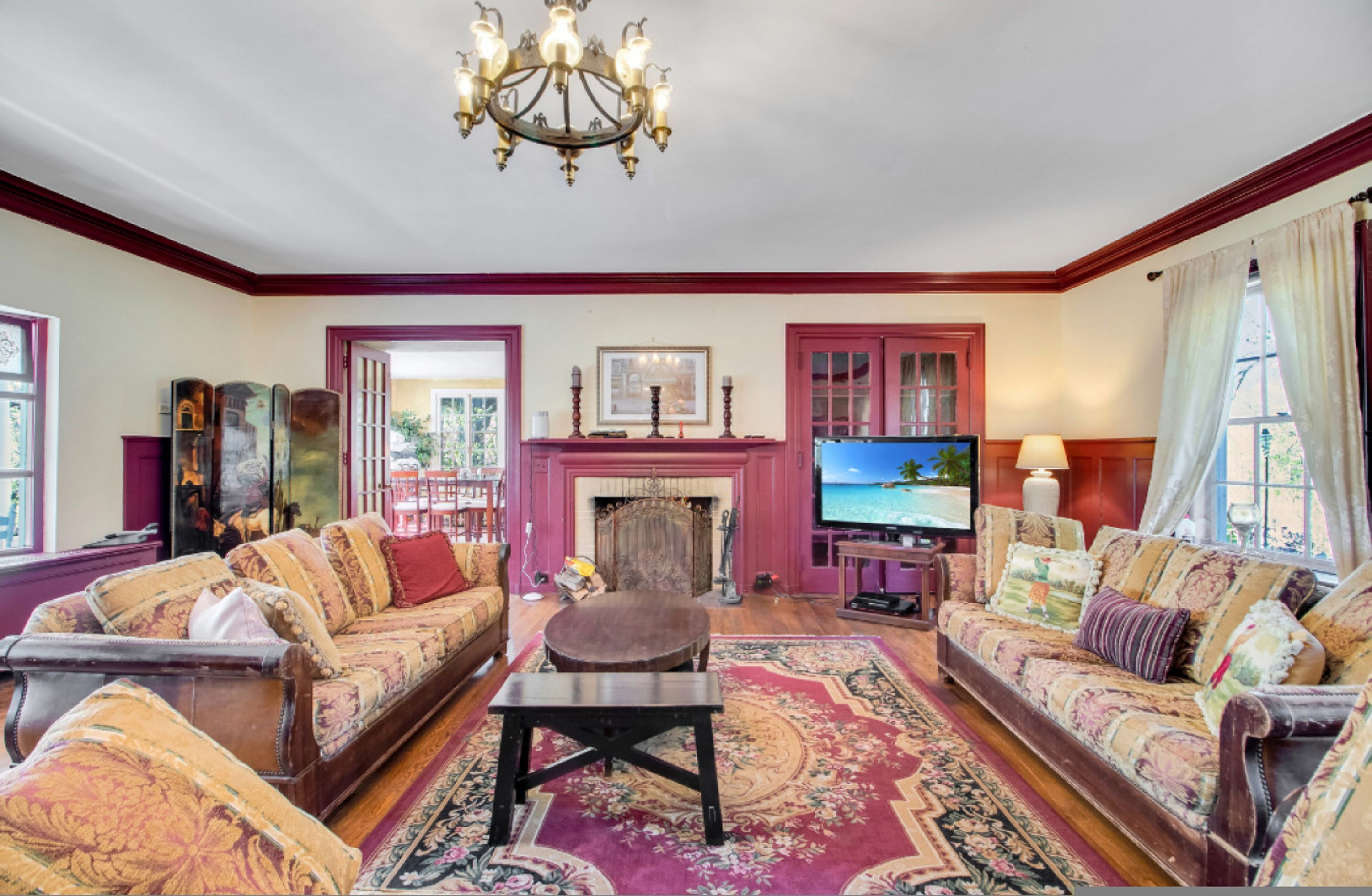 A traditional living room with a fireplace, two sofas, a television, and a chandelier.