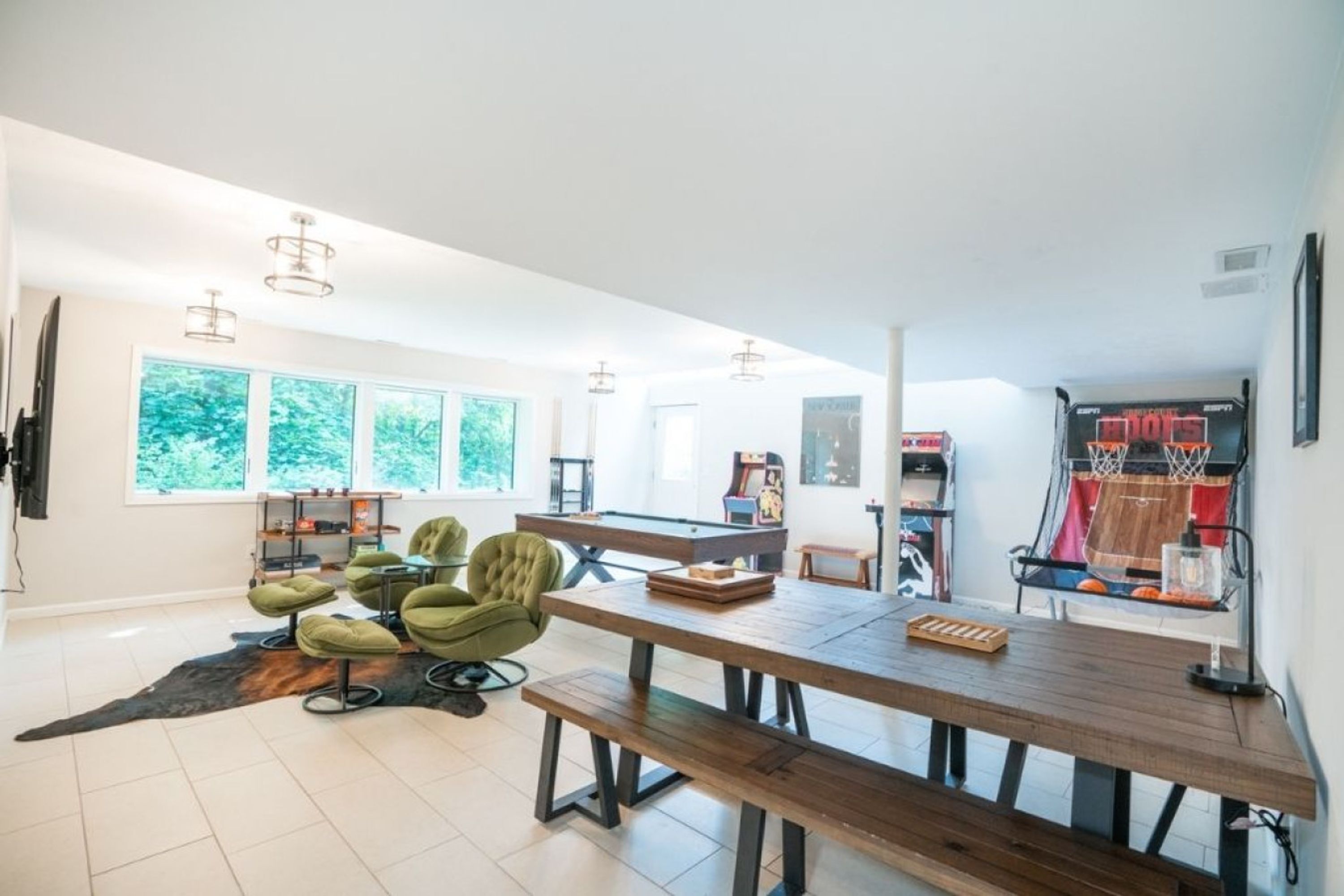 A spacious dining area with a wooden table and green chairs, a pool table, and a basketball hoop.