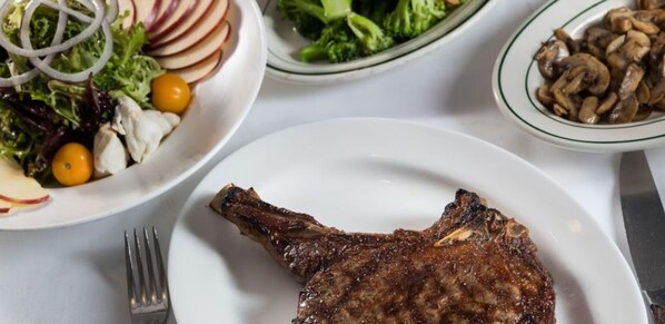 Un plato con un bistec a la parrilla, una ensalada de lechuga, tomates cherry y rábanos, y un tazón de champiñones.