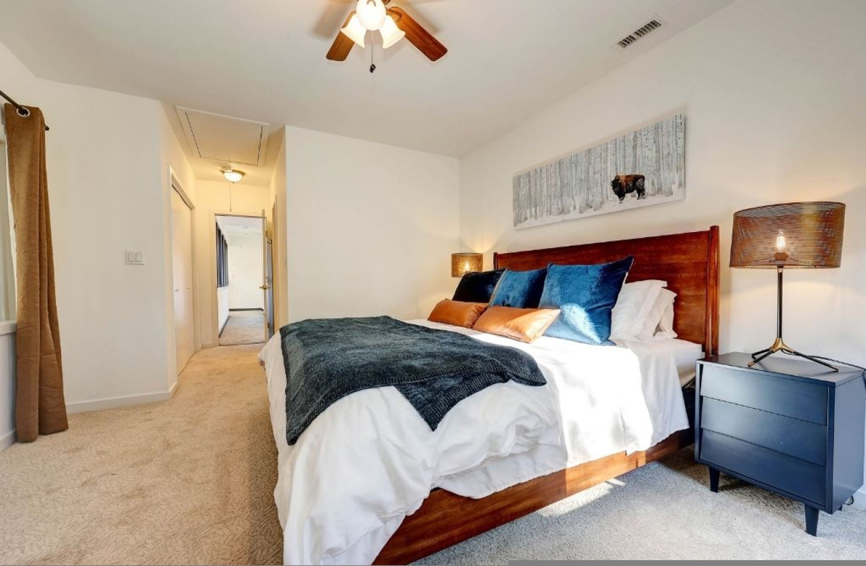 A bedroom with a wooden headboard, a bed with white and brown bedding, a nightstand with a lamp, and a ceiling fan.