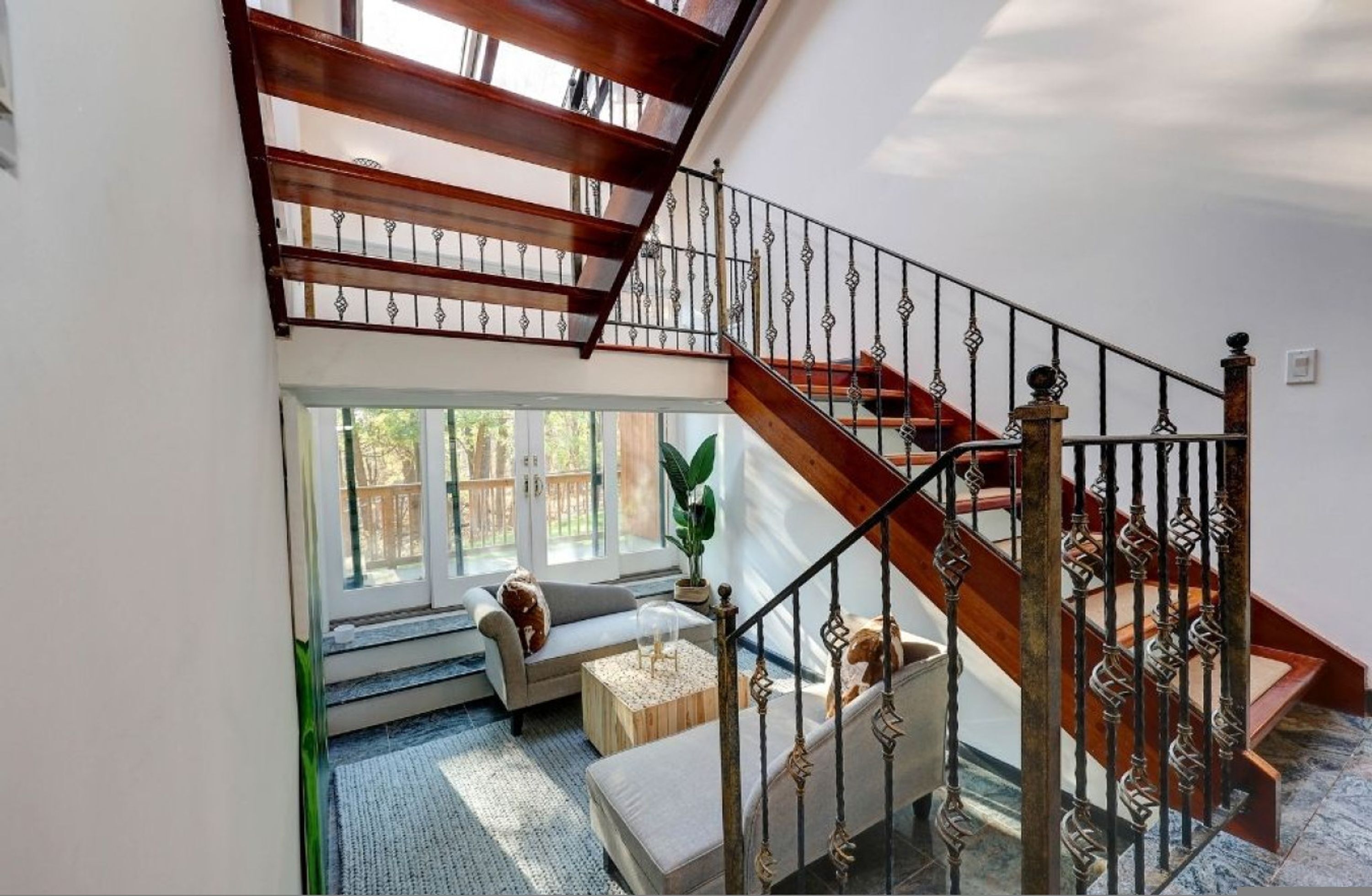 A spacious living area with a wooden staircase, a sofa, a coffee table, and a large window offering a view of the outdoors.