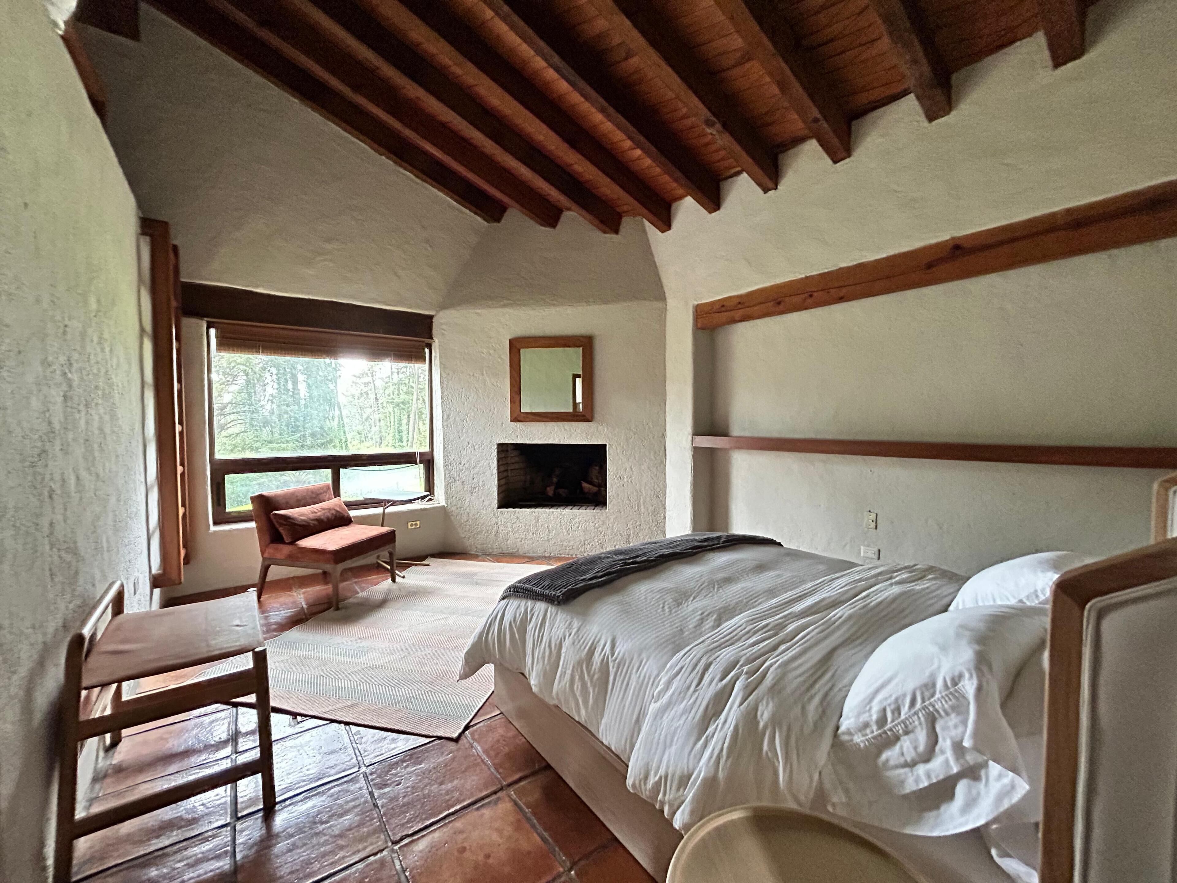 Een slaapkamer met een bed, een stoel, een open haard en een groot raam.