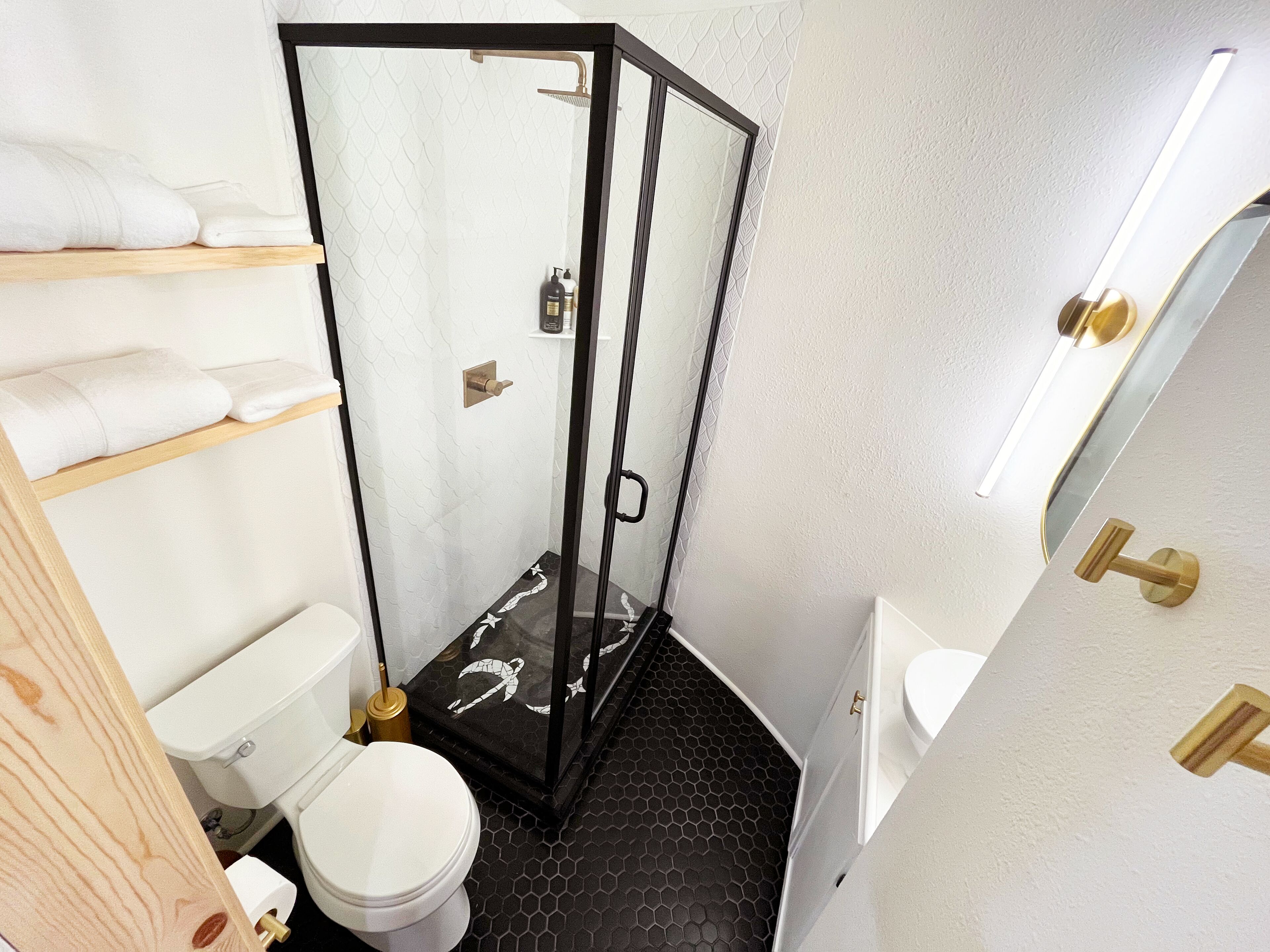 Une salle de bain avec une douche à parois de verre, des toilettes, un lavabo et une étagère avec des serviettes.