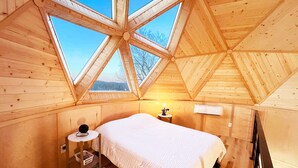 A cozy bedroom with a large bed, a bedside table with a lamp, and a window with a view of trees. - 🌟Planetarium Treehouse🌟Stargazing Observatory with Beaver Lake Views (Springdale)
