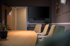 A conference room with a wooden table, four chairs, a flat-screen TV, and a small plant. - Voco Zeal Exeter Science Park (Exeter)
