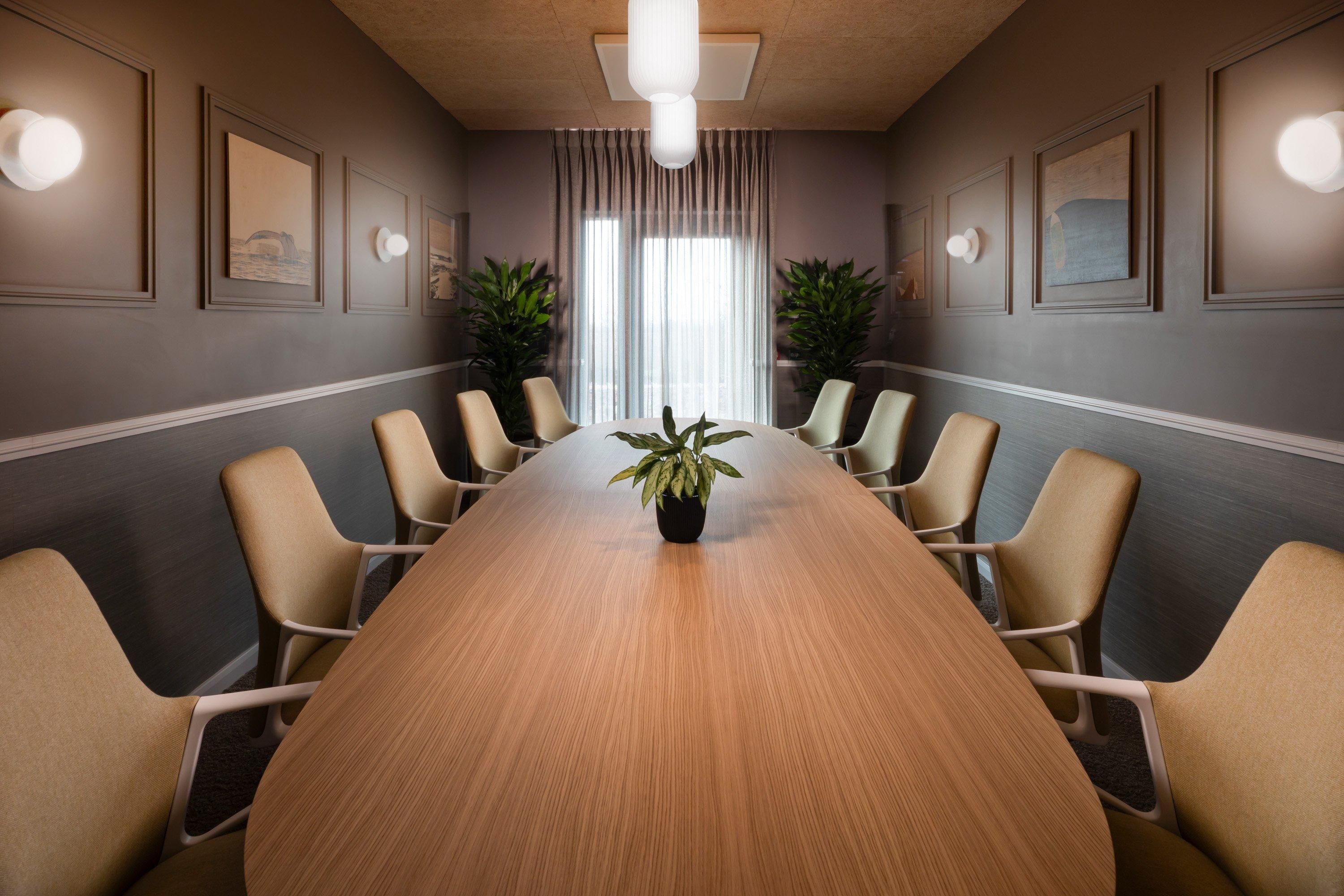 Una sala de conferencias con una larga mesa de madera, sillas color beige, plantas en macetas y obras de arte enmarcadas en las paredes.
