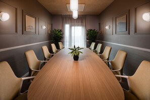 Ett konferensrum med ett långt bord i trä, beige stolar, krukväxter och inramade konstverk på väggarna.