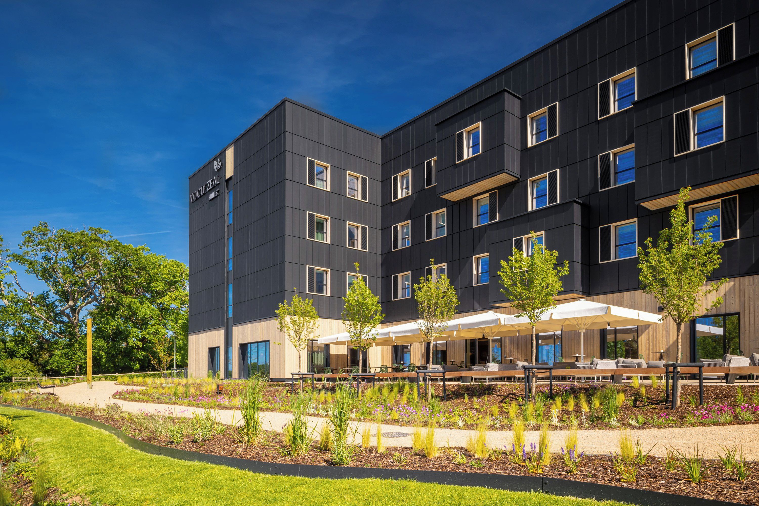 A modern building with a flat roof, multiple windows, and a covered outdoor seating area with tables and chairs.