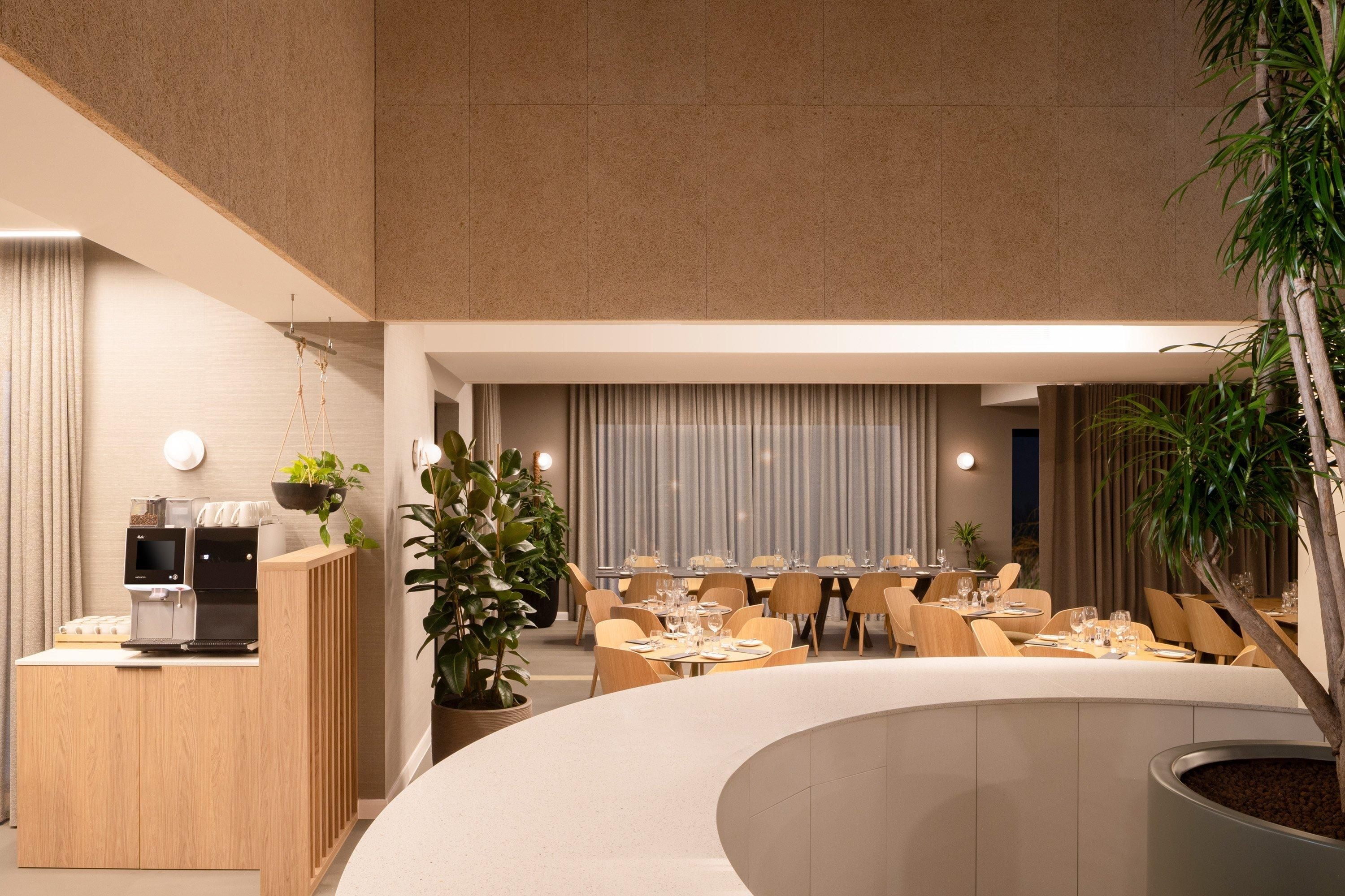 A modern restaurant with a curved seating area, a coffee station, and potted plants.