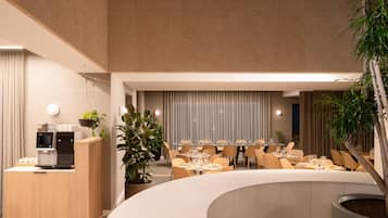 A modern restaurant with a curved seating area, a coffee station, and potted plants.