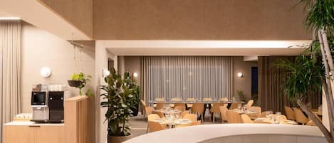 A modern restaurant with a curved seating area, a coffee station, and potted plants.