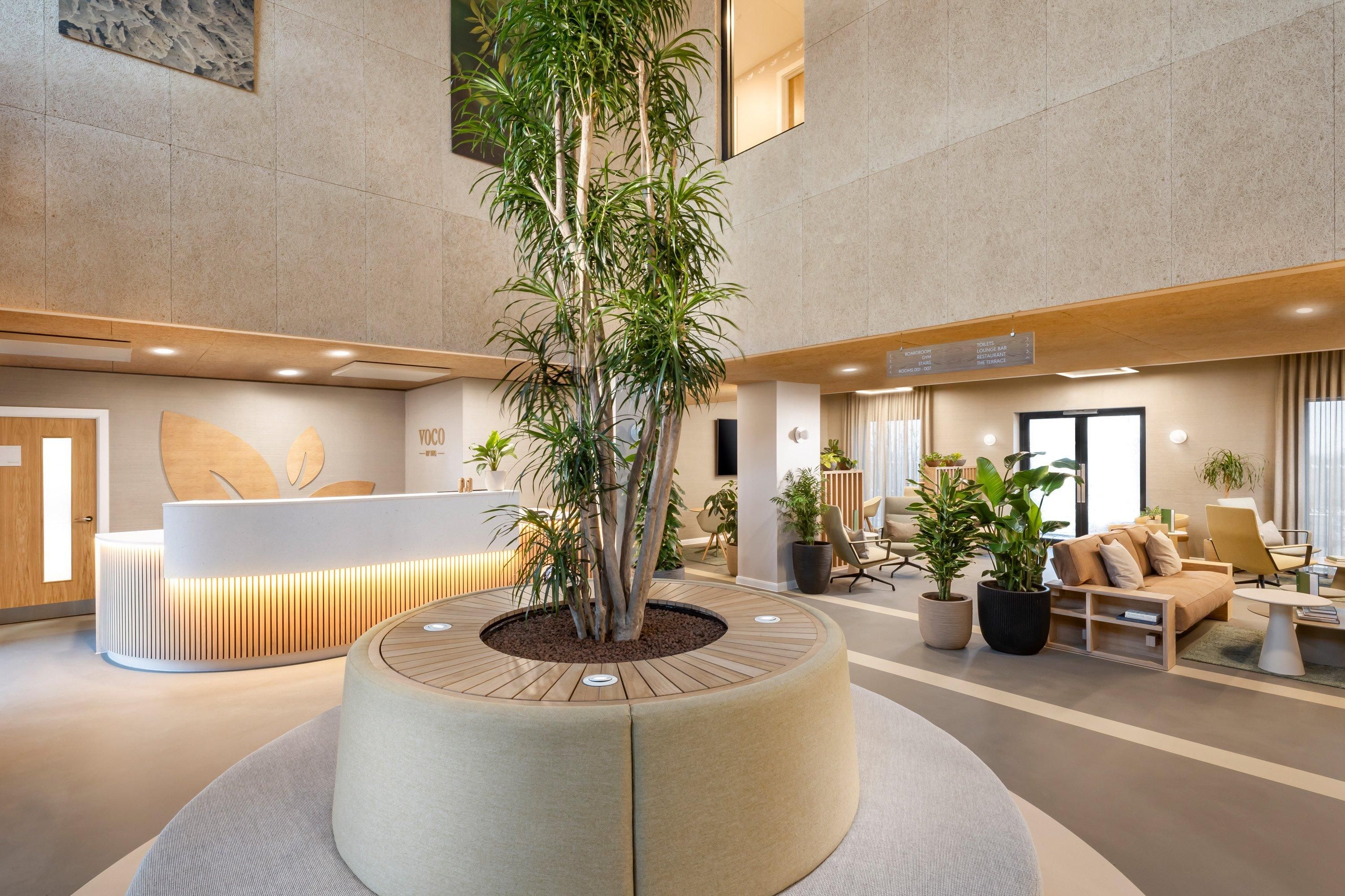 A modern lobby with a central circular planter, a reception desk, seating area, and a large window.