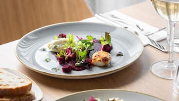 A plate of food with a scallop, greens, and beetroot on a ceramic plate.