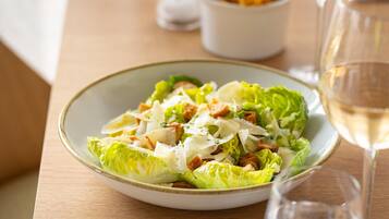 Ensalada César con crutones y queso, acompañada de una copa de vino blanco sobre una mesa de madera.