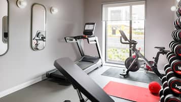 A gym with a treadmill, bench, dumbbells, and a red mat.