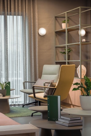 A modern office space with a comfortable chair, a bookshelf, and a small table with books and a plant. - Voco Zeal Exeter Science Park (Exeter)
