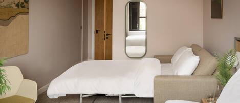 Un dormitorio con cama, sofá, sillón, espejo y puerta.