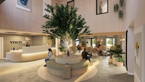 Un moderno vestíbulo de hotel con una palmera central, mostrador de recepción, zonas de estar y obras de arte en las paredes.