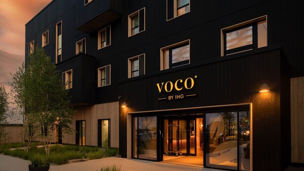 Un edificio moderno con fachada oscura y múltiples ventanas. El nombre "VOCO" se muestra destacadamente sobre la entrada.