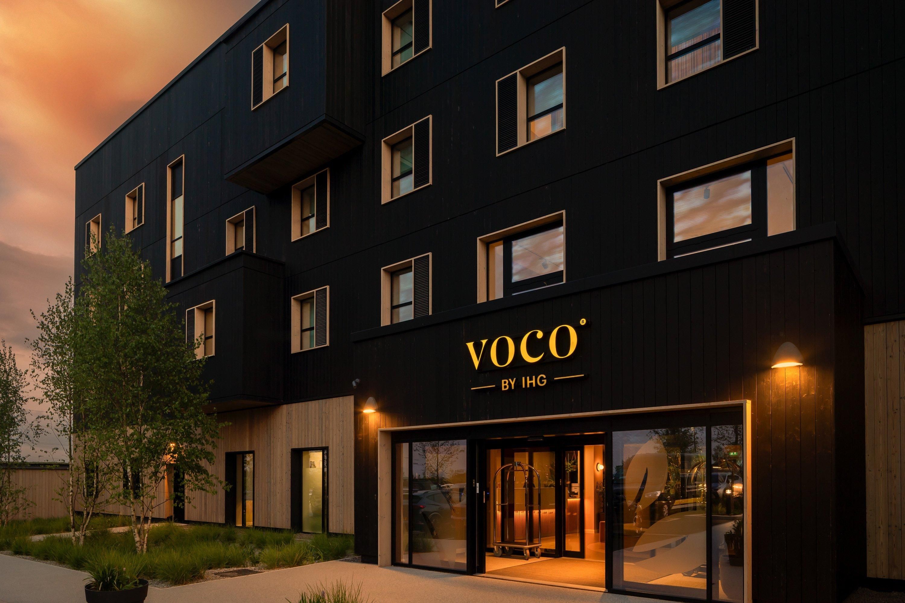 Um edifício moderno com fachada escura e várias janelas. O nome "VOCO" está em destaque acima da entrada.