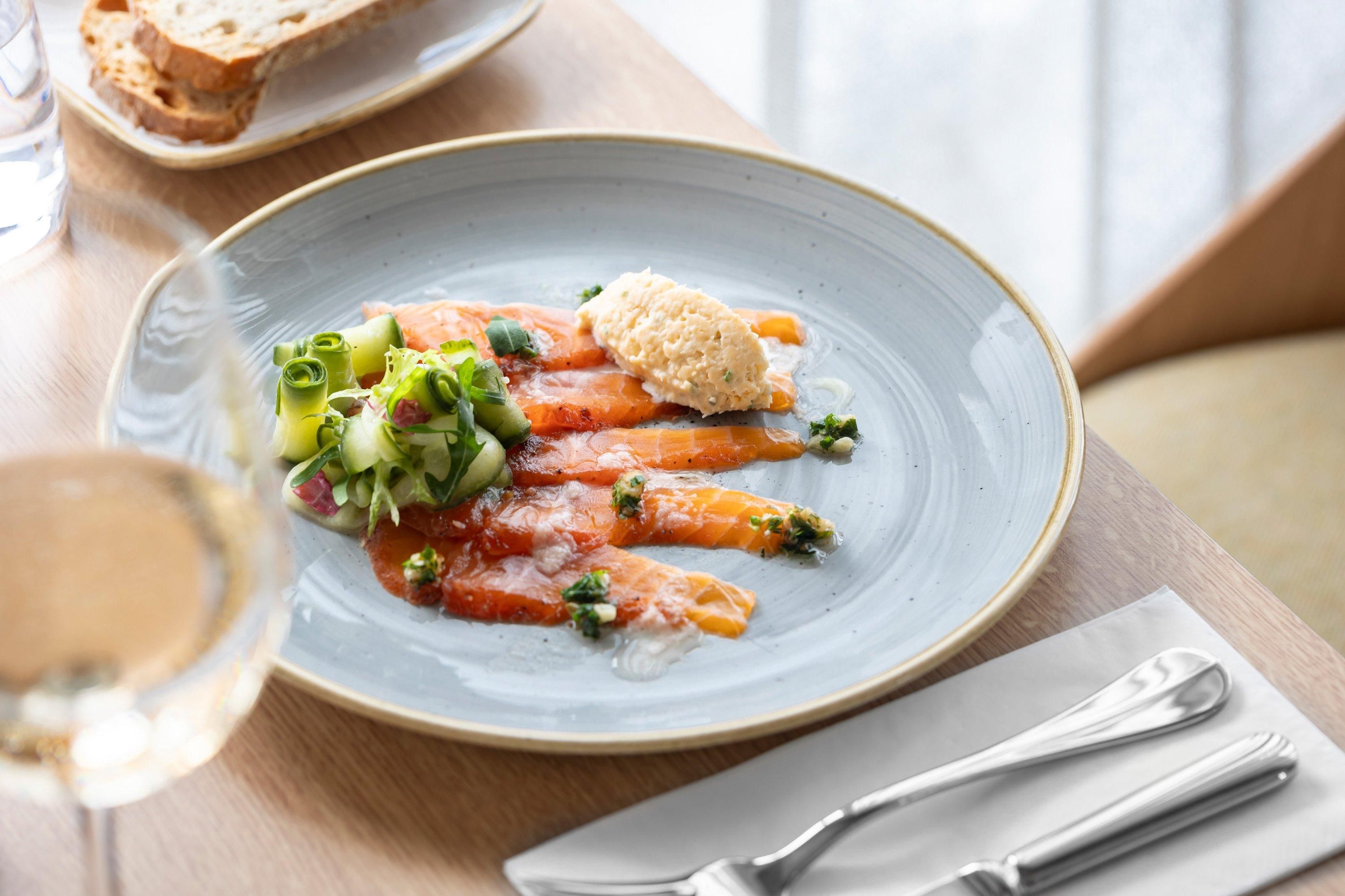 Un plato de comida con salmón, vegetales verdes y una cucharada de salsa sobre un plato de cerámica.